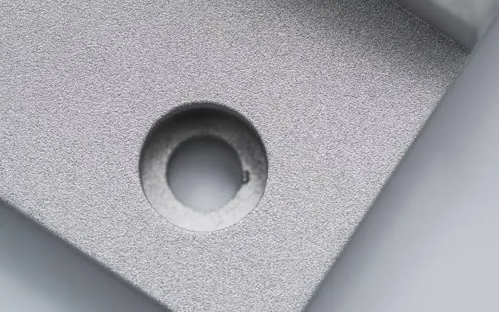 Bead blasted aluminum surface with a uniform matte texture around a machined hole