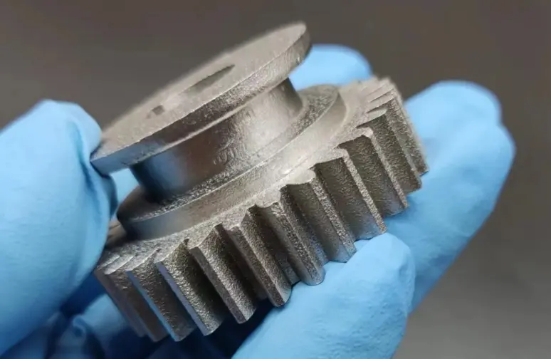 3D printed metal gear with precision teeth held by a gloved hand