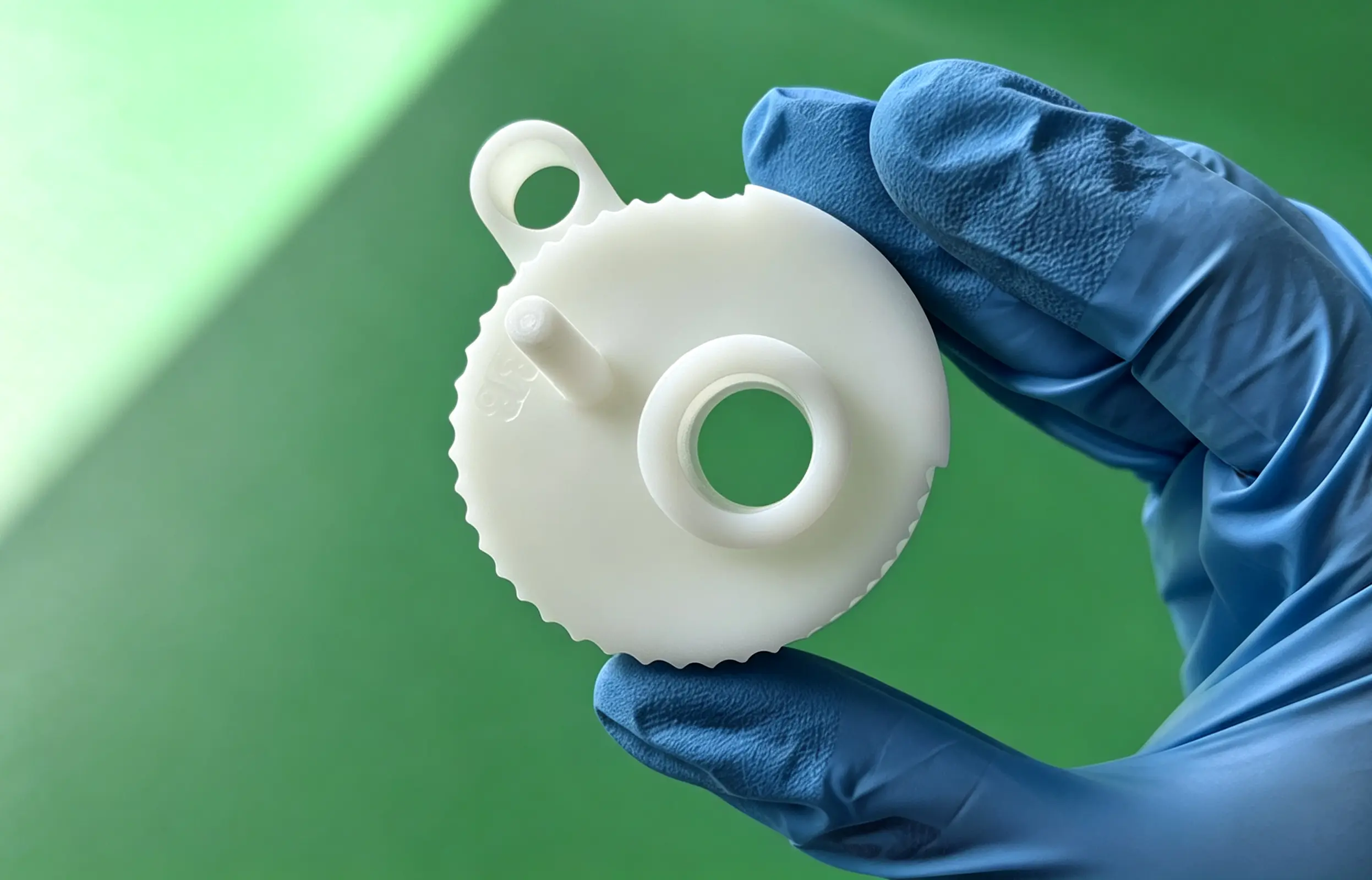 A white 3D-printed plastic component with a smooth matte surface, held by a hand wearing a blue protective glove.