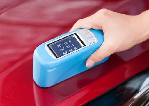 Digital gloss meter measuring the gloss level of a red automotive paint surface